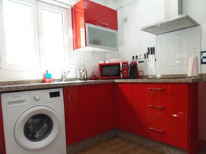 Une cuisine avec des placards rouges, un four à micro-ondes, une machine à café et un lave-linge.