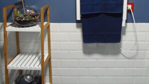 A bathroom with a blue towel hanging on a white towel rack, a shelf with a small plant and a sign that says "HOLA!", and a white tiled wall. - Beautiful studio in Triana (Sevilla)