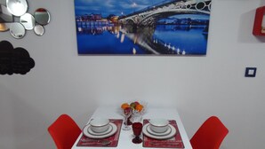 A dining area with a table set for two, a red chair, a white tablecloth, and a painting of a bridge on the wall. - Beautiful studio in Triana (Sevilla)