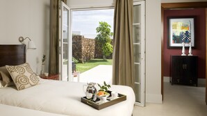 A hotel room with a bed, a tray with a coffee pot, cups, and a fruit bowl. The room has a view of a garden and a stone wall. - Modern Villa with Heated Pool, Wifi and Air Conditioning in Los Mojones (Puerto del Carmen)