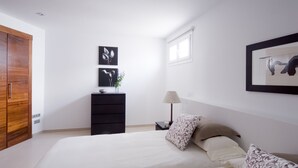 A bedroom with a large bed, a wooden wardrobe, a nightstand with a lamp, and wall art. - Modern Villa with Heated Pool, Wifi and Air Conditioning in Los Mojones (Puerto del Carmen)