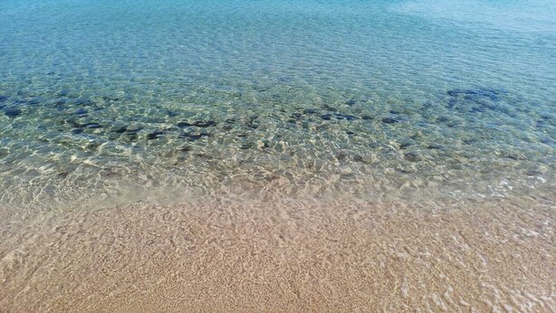 Ein breiter, offener Strand mit sichtbaren Unterwasserfelsen und einer Person im Wasser.