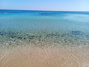 Une plage aux eaux claires où l’on peut apercevoir des rochers sous la surface, et une personne qui s’y trouve.