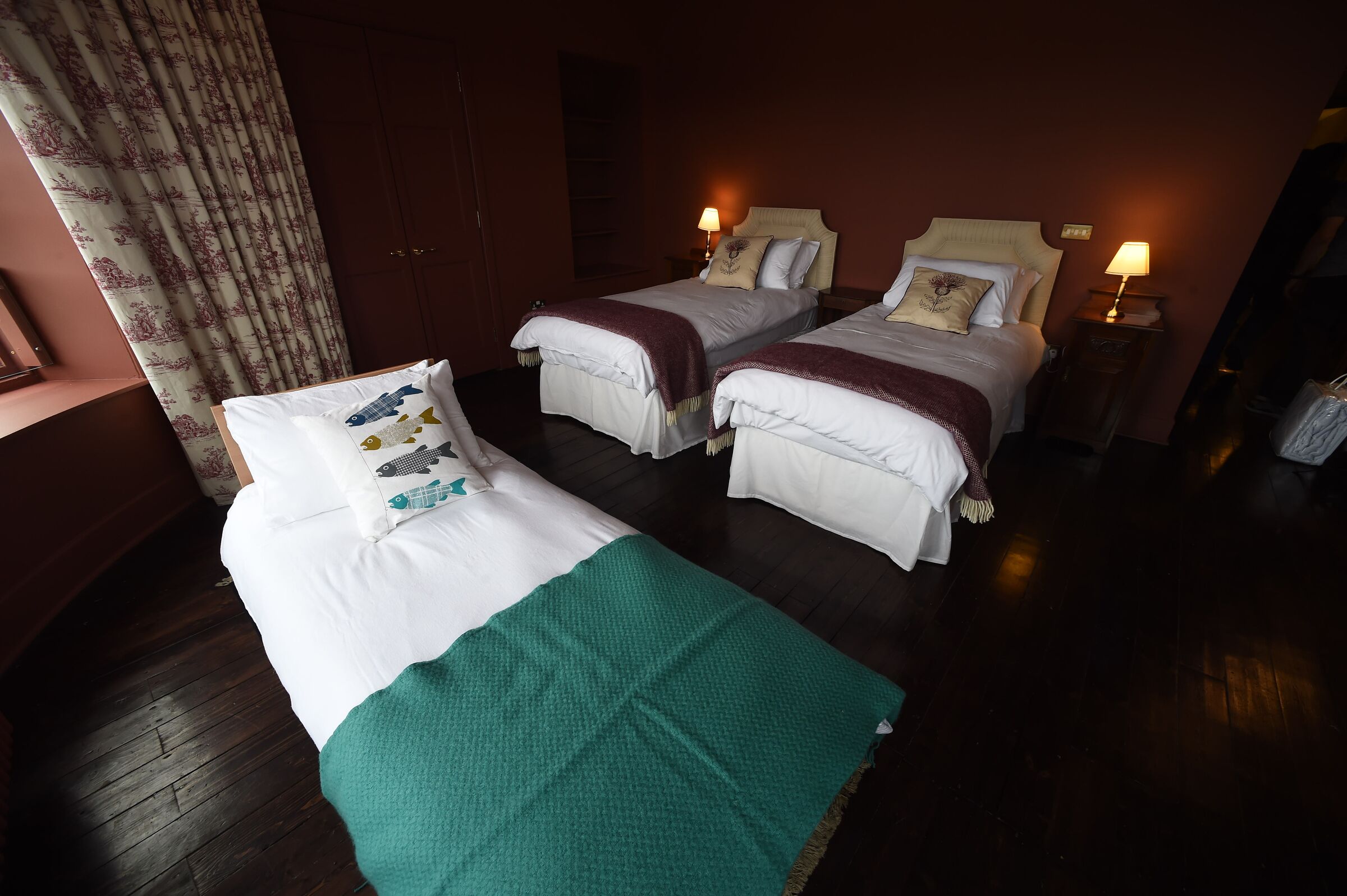 A hotel room with two single beds, a green blanket on one bed, and a wooden floor.