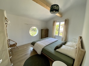 Une chambre à coucher avec un lit, une fenêtre ronde, une armoire et un luminaire suspendu.