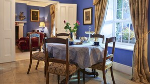 Un comedor con mantel a cuadros, sillas de madera, un jarrón con flores y una ventana con cortinas.