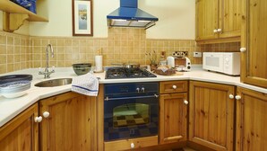 Una cocina con armarios de madera, estufa a gas, horno, microondas y pileta.