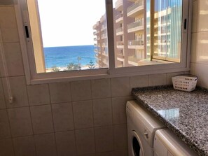A laundry area with a washing machine, a countertop, and a window with a view of the ocean and buildings.