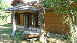 Una cabaña rústica de madera con un porche cubierto y un banco de piedra.