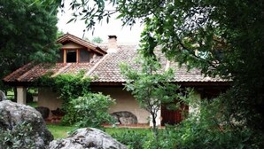Una casa rústica con techo de tejas, rodeada de abundante vegetación y grandes rocas.