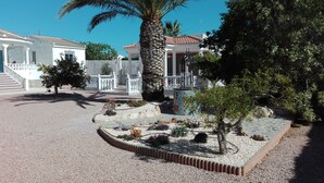 A courtyard with a palm tree, a small garden with flowers, and a white building with a tiled roof. - Beautiful villa with large outdoor kitchen for max. 10 people, swimming pool, air conditioning and wifi (Cdad. Quesada)