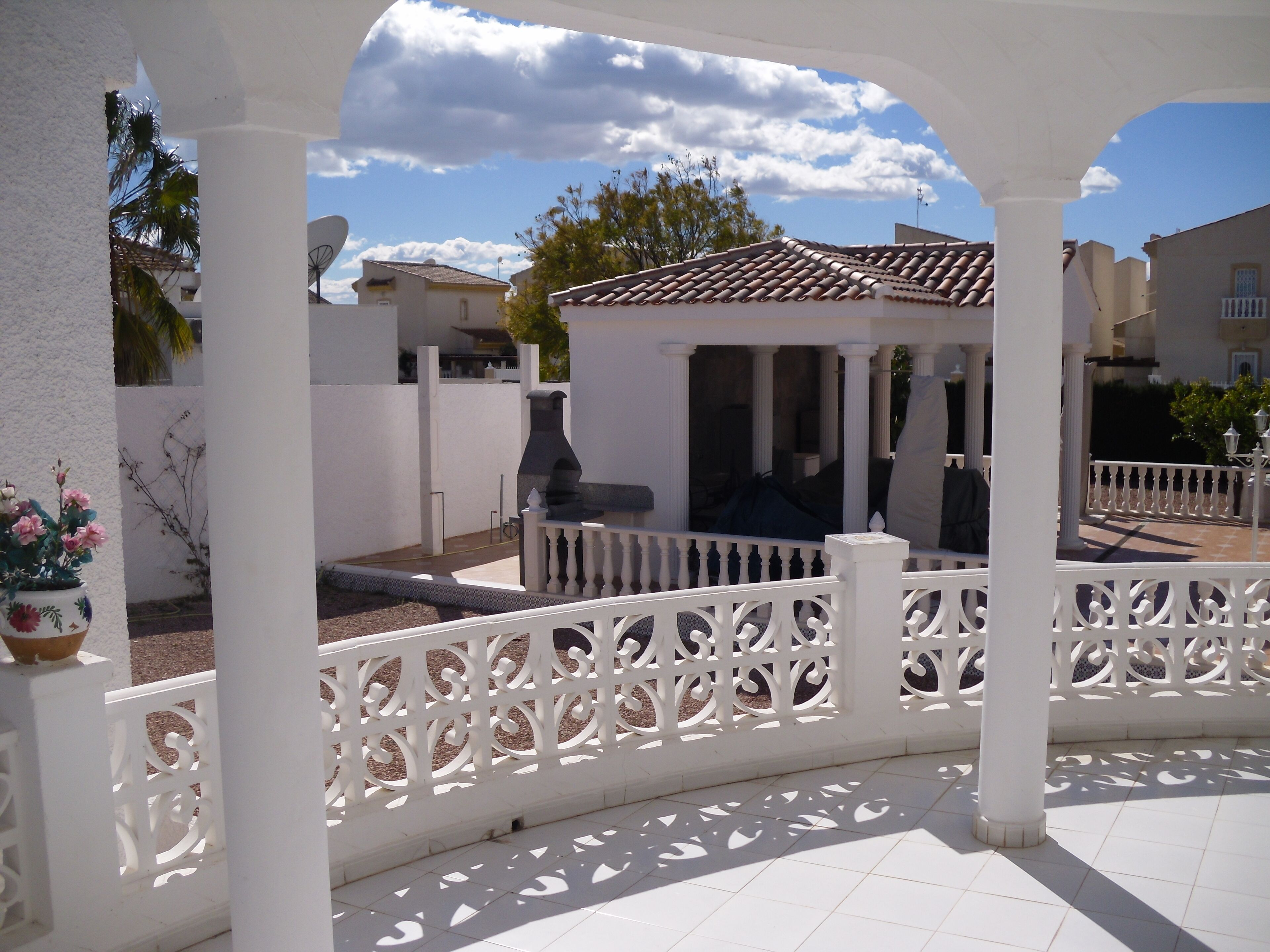 A covered outdoor area with a white fence, a tiled floor, and a small gazebo.