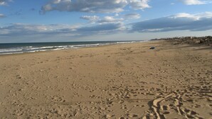 A wide sandy beach with footprints, a wooden fence, and a distant shoreline with buildings. - Beautiful villa with large outdoor kitchen for max. 10 people, swimming pool, air conditioning and wifi (Cdad. Quesada)