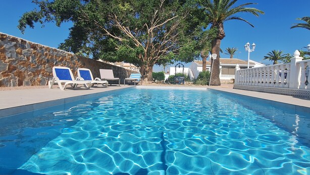 A swimming pool with clear blue water, surrounded by lounge chairs and a stone wall. - Beautiful villa with large outdoor kitchen for max. 10 people, swimming pool, air conditioning and wifi (Cdad. Quesada)