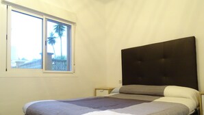 Ein Einzelbett mit dunkel gestaltertem Kopfteil in einem Zimmer mit Fenster.