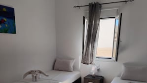 Een kamer met twee bedden, een nachtkastje, een lamp, een raam met gordijnen en een schilderij aan de muur.