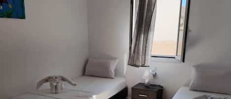 A room with two beds, a nightstand, a lamp, a window with curtains, and a painting on the wall.