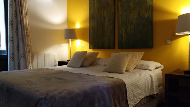 A hotel room with a bed, two bedside lamps, a radiator, and a large painting on the wall. - Casiopea charming lodging for two persons (Braojos)