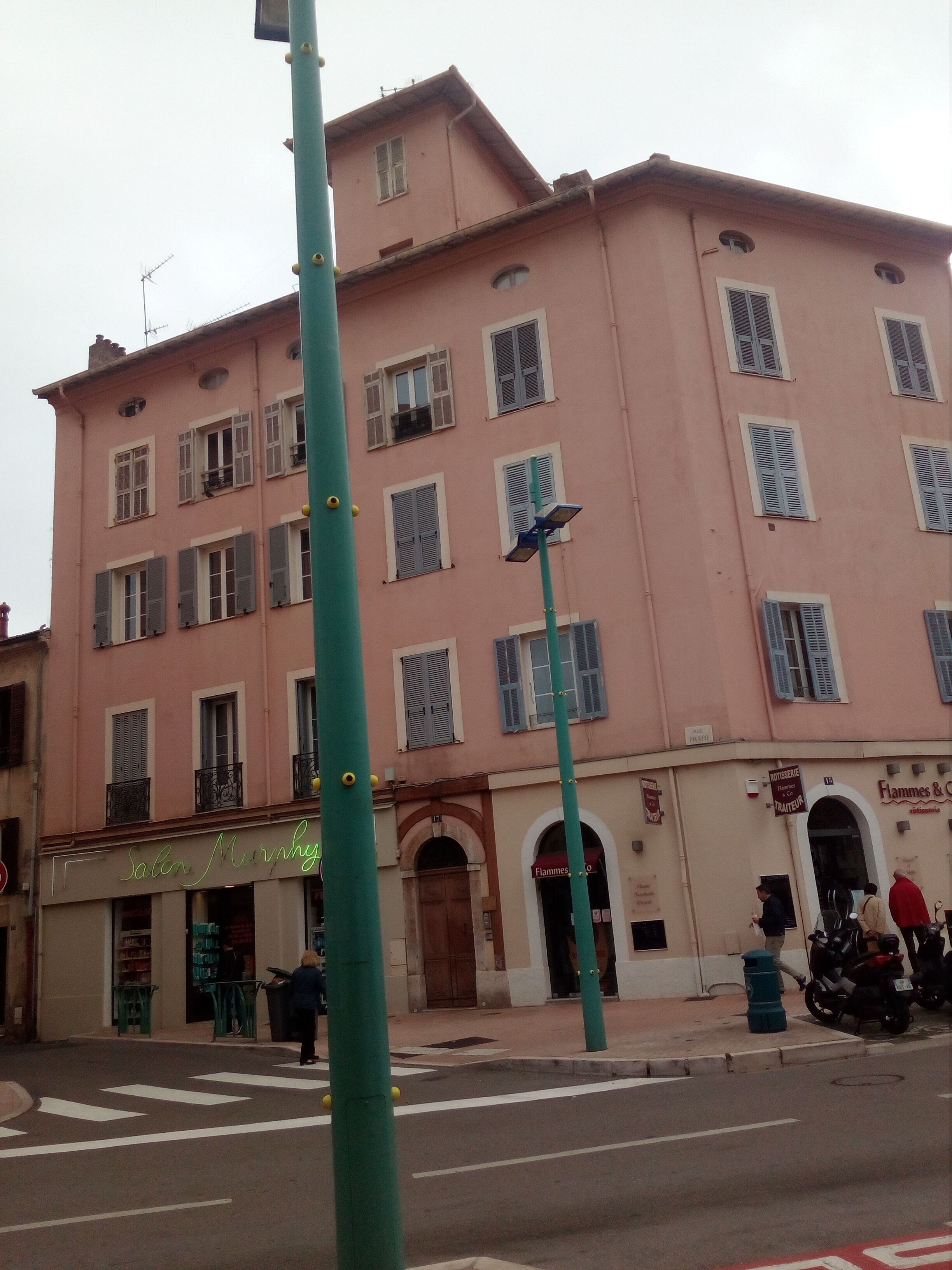 Ein mehrstöckiges Gebäude mit rosa Fassade, ein sichtbarer Laden mit einem Schild und eine Straße mit Fußgängerüberweg.