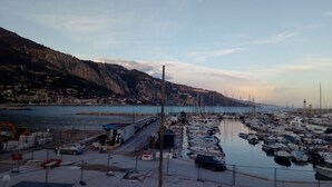Un puerto deportivo con barcos amarrados, una carretera que conduce al agua y montañas al fondo.