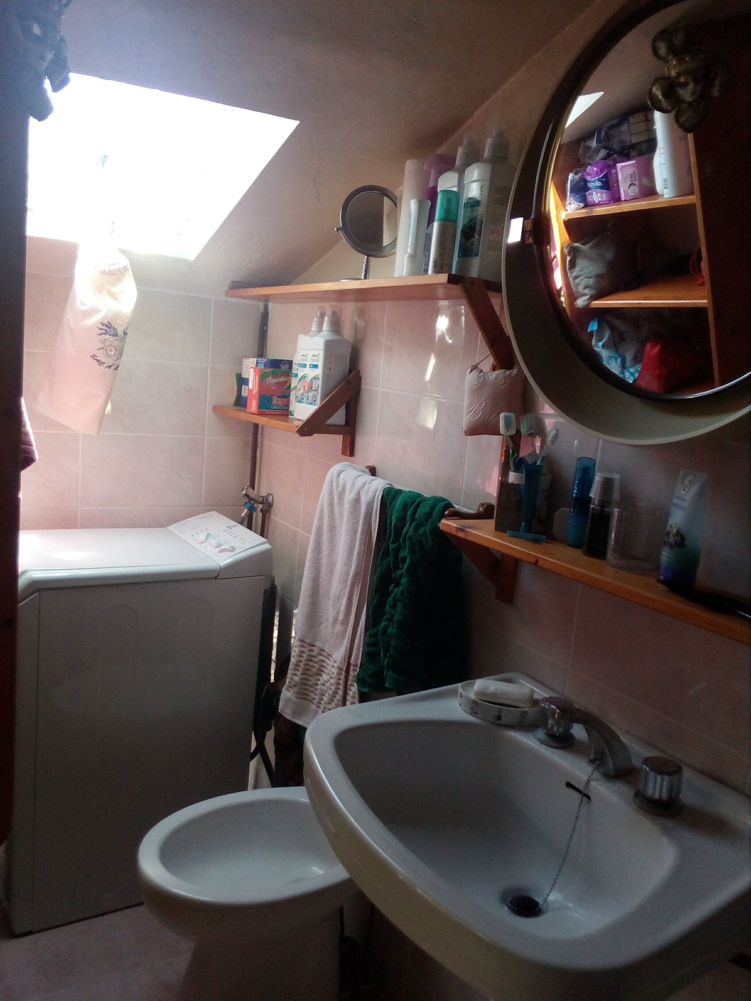 A compact bathroom with a washing machine, a sink, and shelves with toiletries.