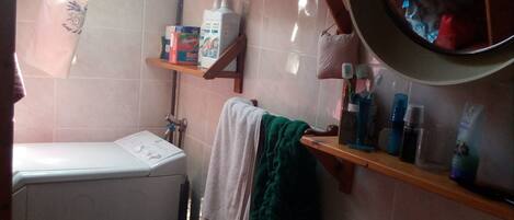 A compact bathroom with a washing machine, a sink, and shelves with toiletries.