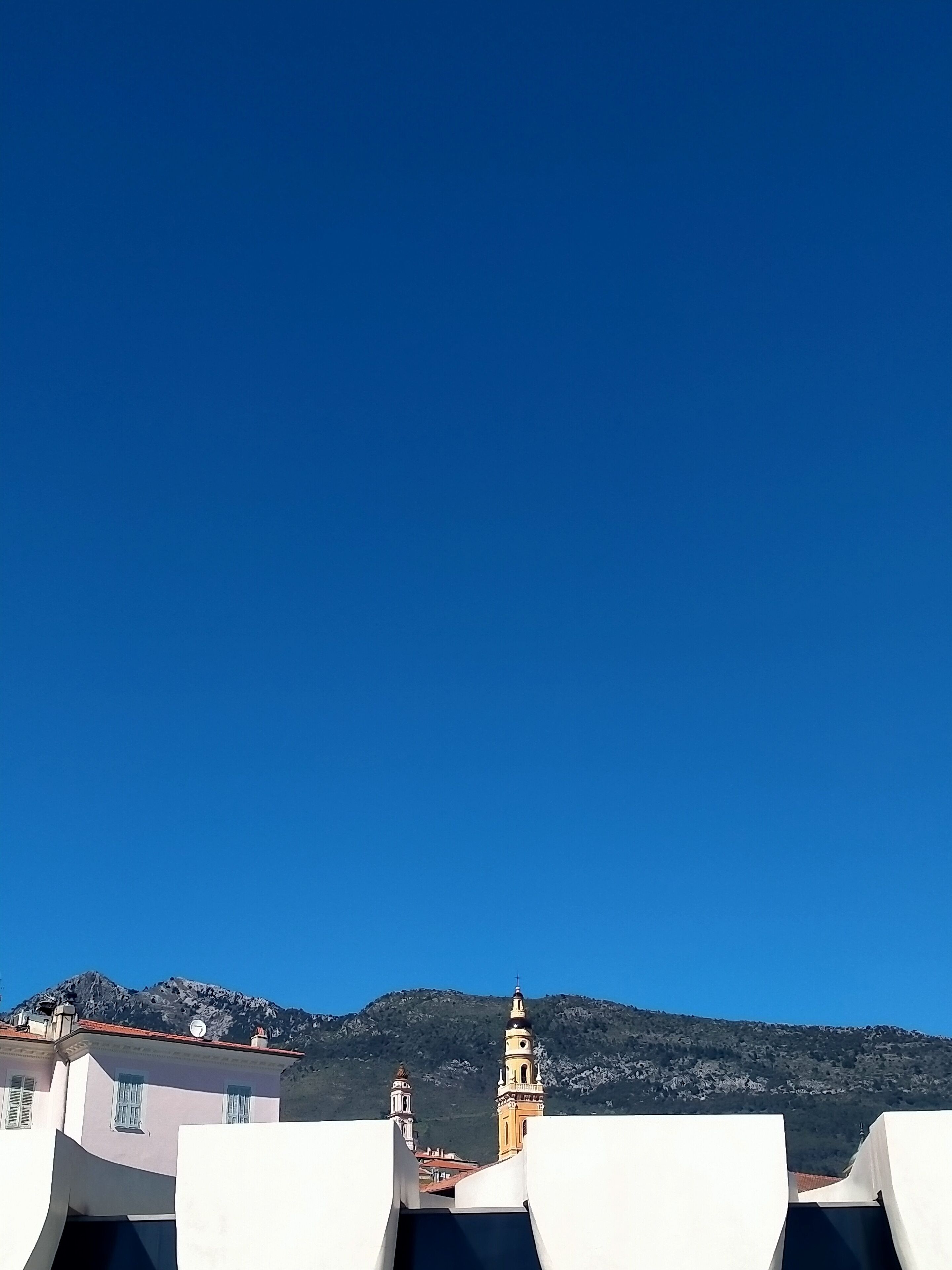 A building with a flat roof and a bell tower, set against a mountainous backdrop.