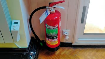 A fire extinguisher mounted on a wall, a digital thermostat, and a sign indicating a fire exit.