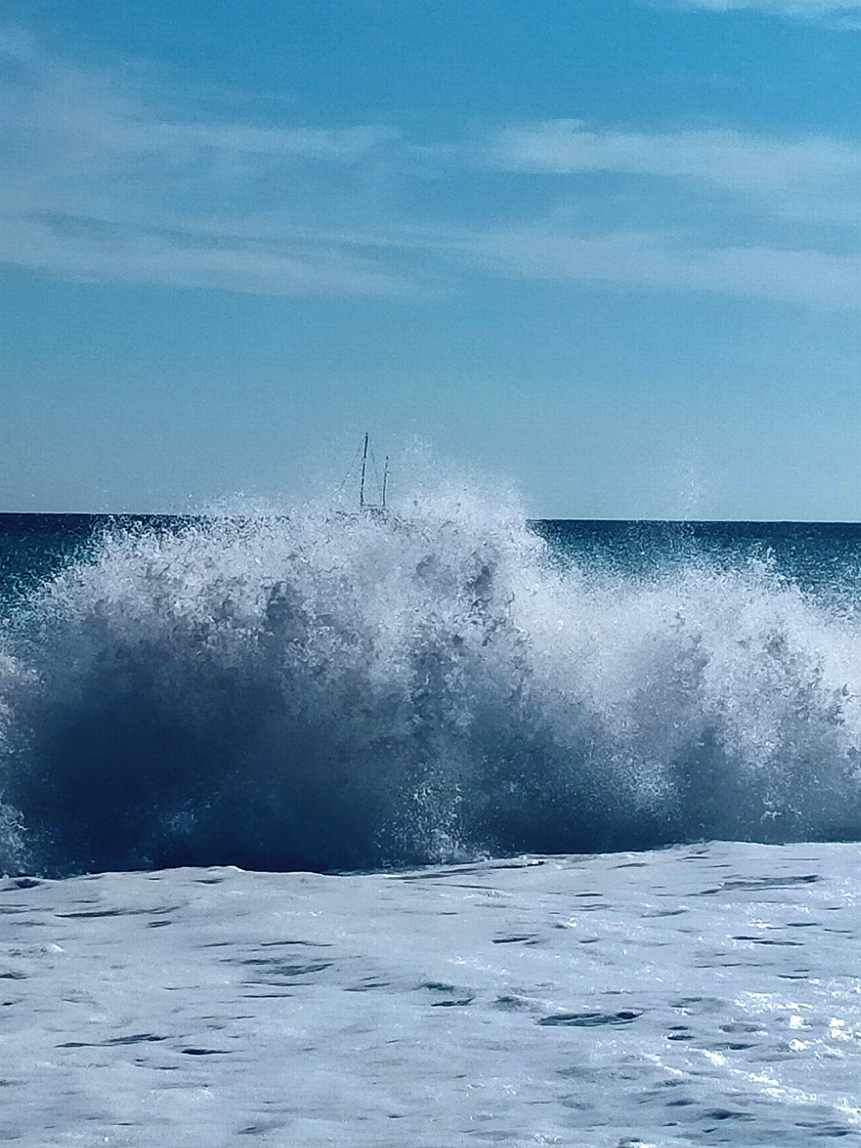A large wave crashing onto a beach with a clear sky in the background.