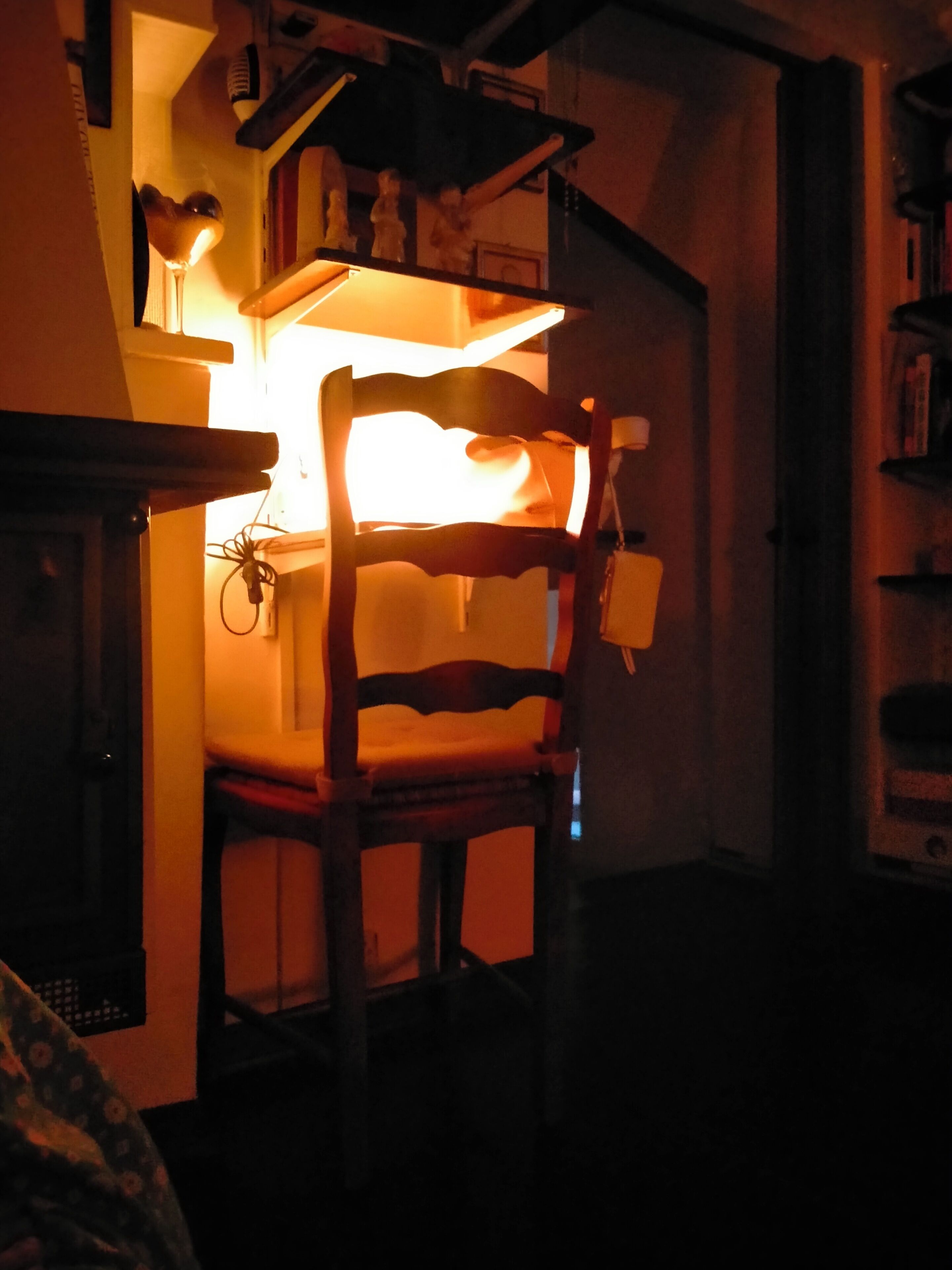 Une chaise dans une pièce faiblement éclairée, avec une étagère au-dessus.