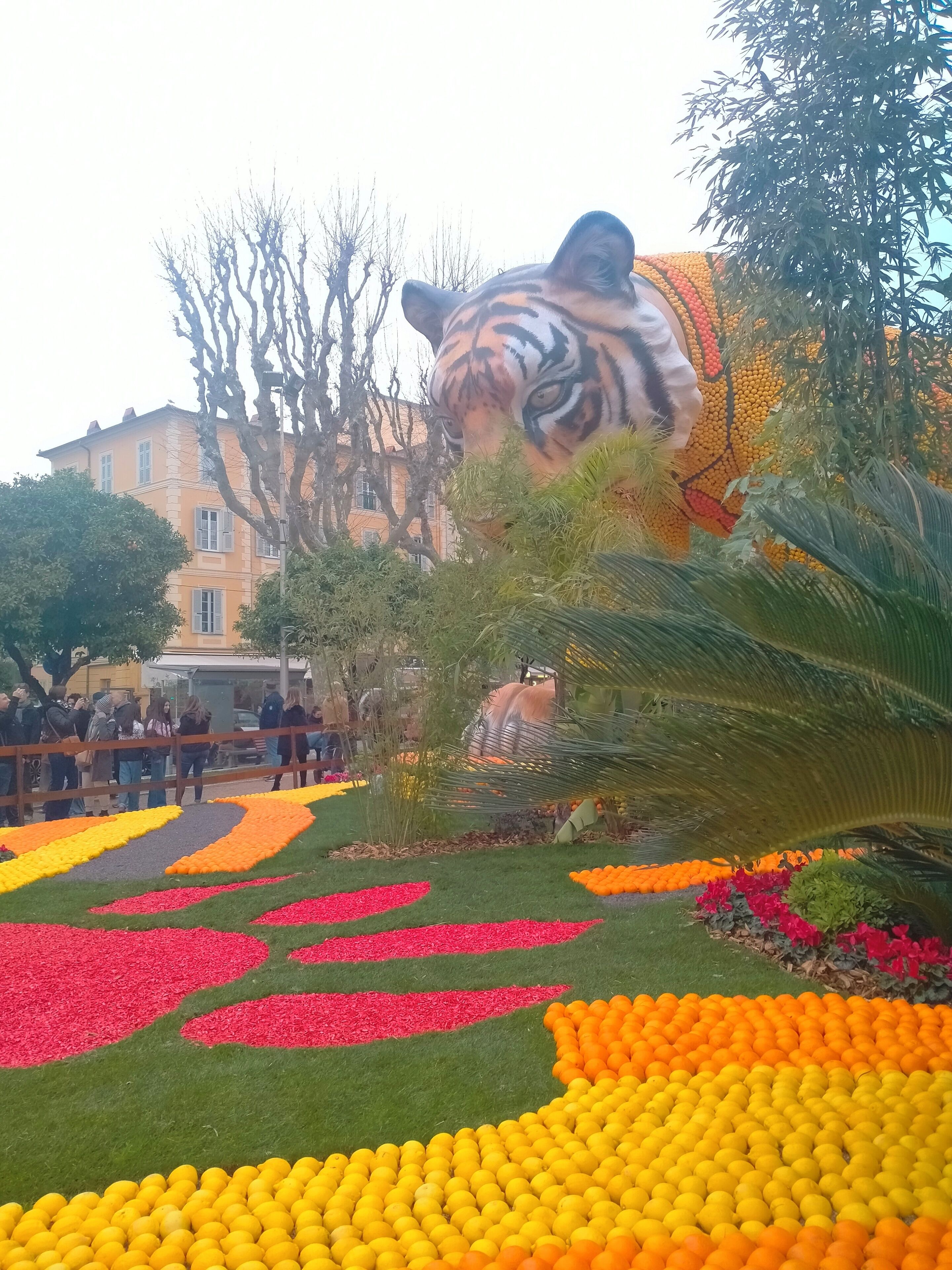 A garden with a large tiger statue, a building in the background, and a crowd of people.