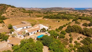 En hvid villa med swimmingpool, omgivet af bakker og grøn bevoksning.