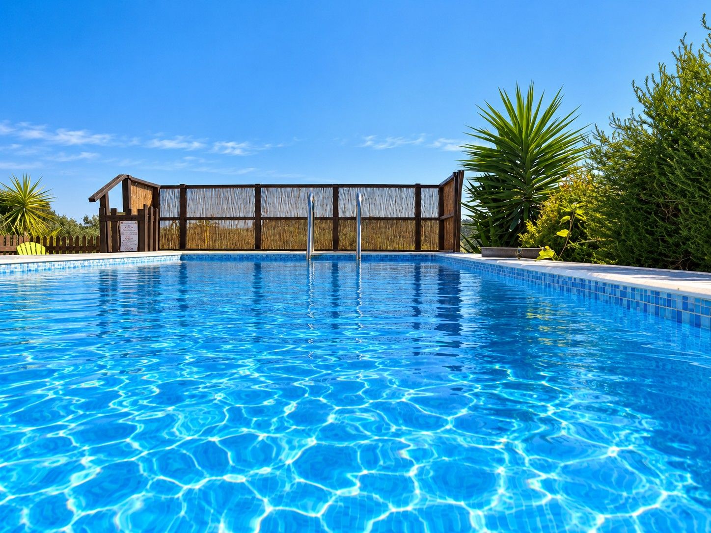 Piscina azul límpida com cerca de madeira e plantas tropicais ao redor.