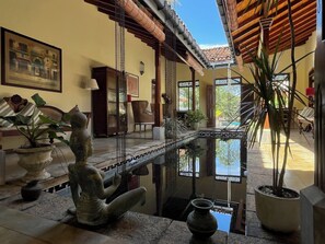 Un interior tradicional con una estatua de piedra, una pequeña piscina y plantas en macetas.