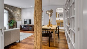 Un salon moderne avec un mur en pierre, un plancher en bois, un coin repas avec une table et des chaises en bois, et un téléviseur posé sur un meuble en bois.