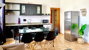 A modern kitchen with a dining area, featuring a stainless steel refrigerator, a microwave, and a glass-top dining table with black chairs. - SENSES WELLNESS APARTMENT BUILDING (Tarifa)