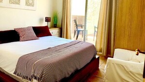 A hotel room with a large bed, a small table with a plant, a chair, and a view of the outside balcony. - SENSES WELLNESS APARTMENT BUILDING (Tarifa)