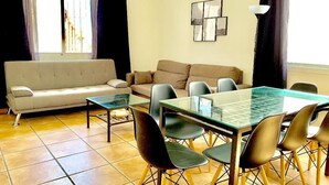 A living room with a glass-top dining table, black chairs, a beige sofa, and a white couch. - SENSES WELLNESS APARTMENT BUILDING (Tarifa)