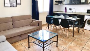 A modern living room with a sofa, a glass coffee table, and a dining area with chairs and a table. - SENSES WELLNESS APARTMENT BUILDING (Tarifa)