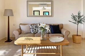 A living room with a sofa, a coffee table, a lamp, a mirror, and a potted plant.