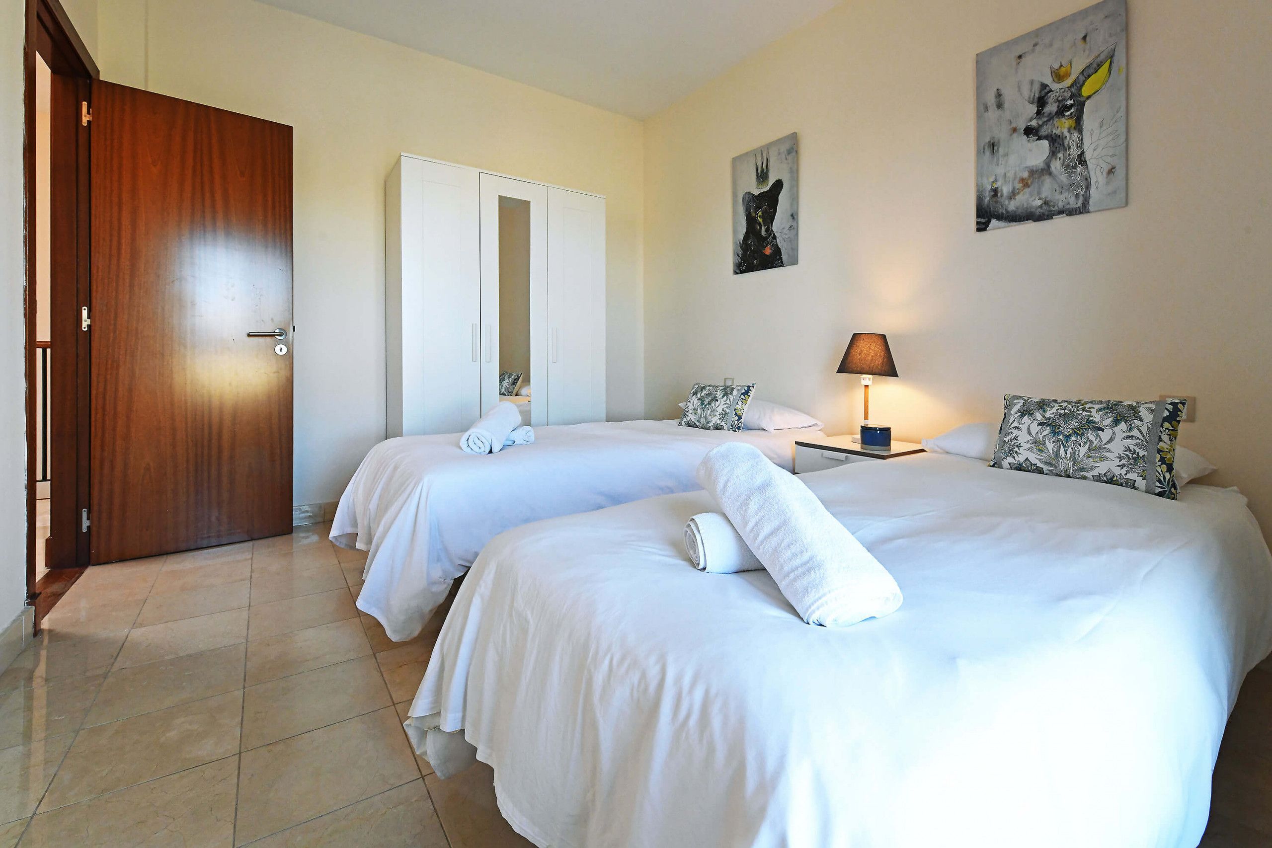 Habitación de hotel con dos camas, un armario y dos cuadros en la pared.