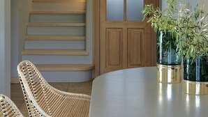 Una escalera con escalones de madera y una puerta de vidrio. Hay sillas de mimbre y una mesa con una planta.