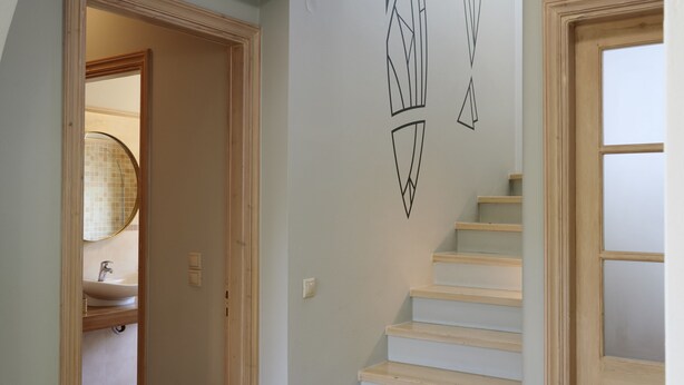 Un escalier avec une rampe et des marches de couleur claire, menant à une pièce dotée d’une porte en bois et d’une petite fenêtre.