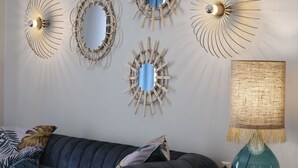 Una sala de estar moderna con un sofá azul oscuro, varios espejos en la pared y una lámpara sobre una mesita de madera.