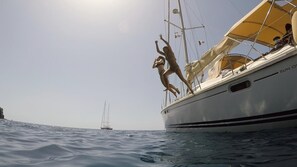 A sailboat with a person standing on the deck, another person on the bow, and a distant sailboat. - RENT LUXURY Sailingboat in GREECE, CYCLADES & DODECANESE, with skipper & CHEF (Mykonos)