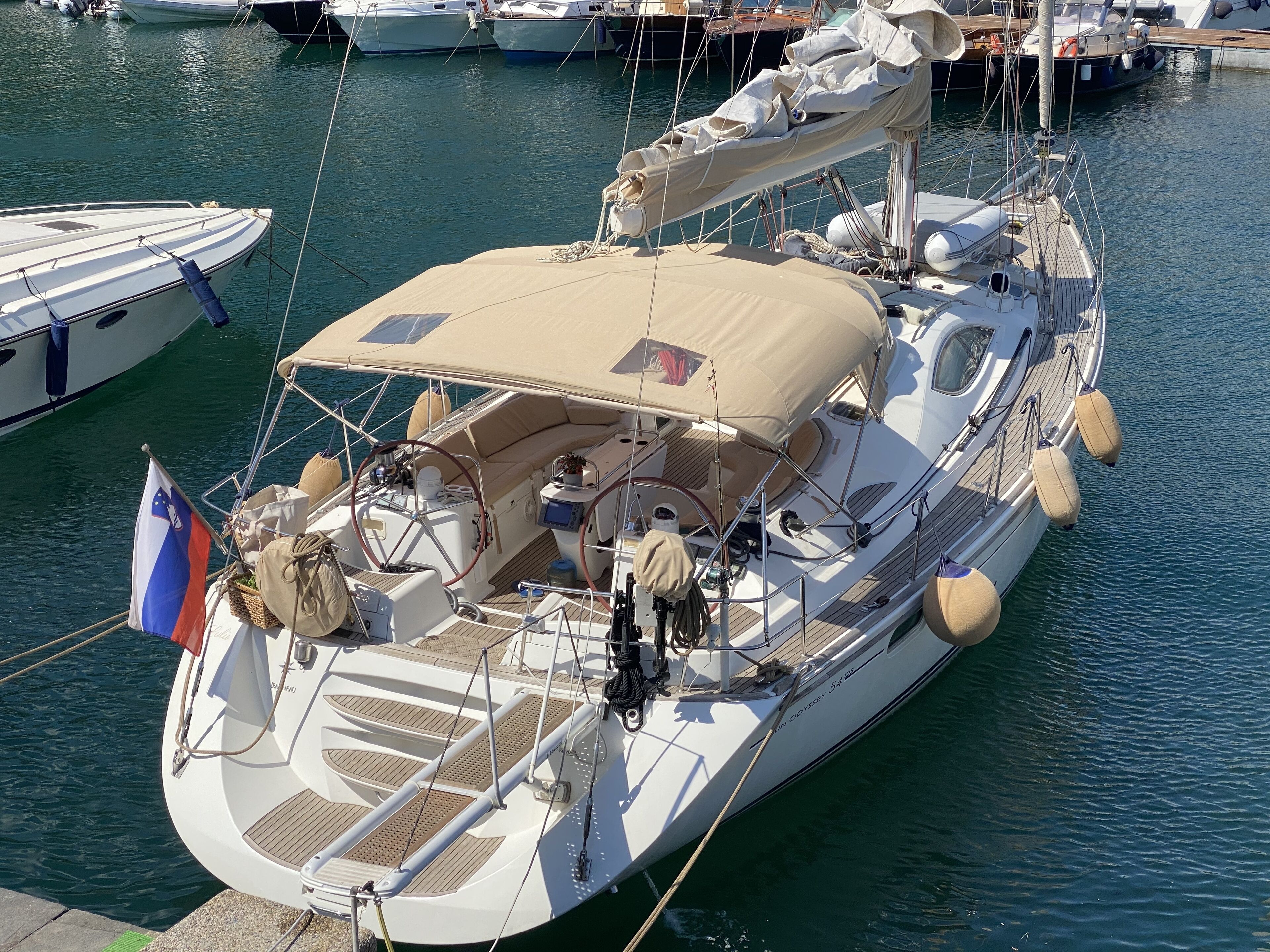 A yacht docked at a marina with a covered deck, multiple seating areas, and a flag.