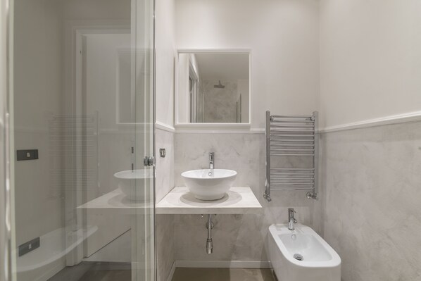 Een moderne badkamer met een douchecabine van glas, een wastafel met twee kommen en een bidet.