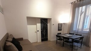 A living room with a sofa, a dining table with chairs, a door, and a window with curtains. - Prestigious "farnese loft" (Roma)