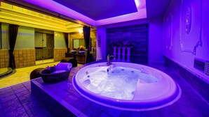 Un moderno spa con una bañera grande, una zona de estar con un cesto de toallas y una pared de piedra con chimenea.