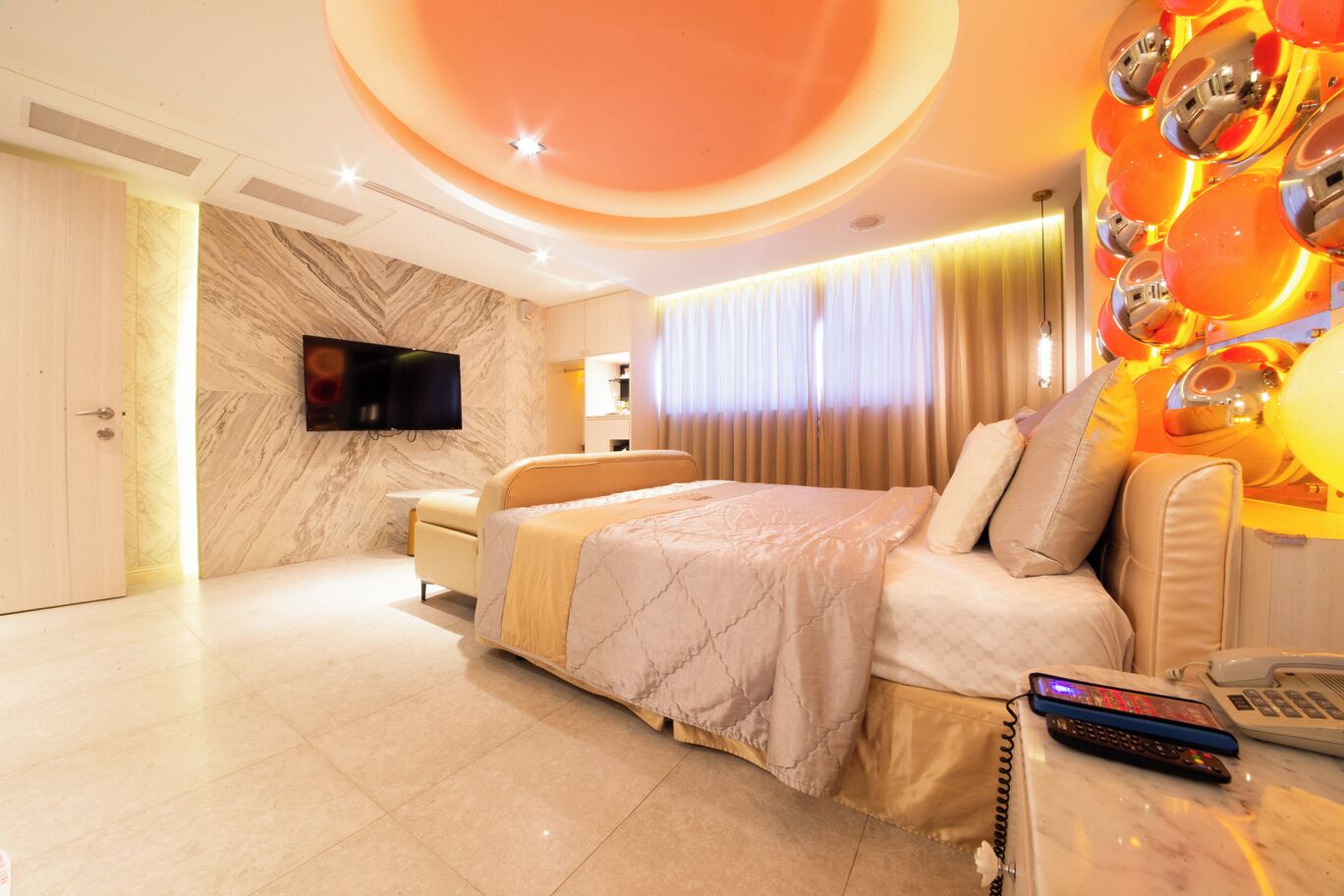 Una habitación de hotel moderna con una cama grande, un televisor, un escritorio con teléfono y una lámpara fijada a la pared.